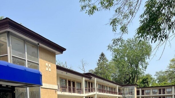A motel with a parking lot, multiple-story buildings, and a blue awning over the entrance.