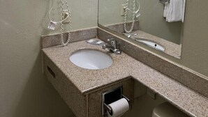 A bathroom with a sink, two hair dryers, a mirror, and a toilet.