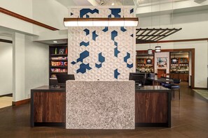 A reception desk with a patterned wall, a wooden counter, and a seating area with chairs. - Candlewood Suites Cincinnati Northeast - Mason (Mason)