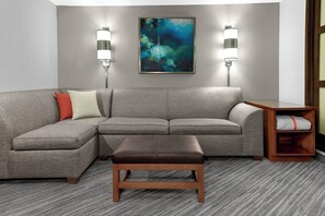 Una sala de estar moderna con un sofá modular gris, un banco de madera y dos lámparas fijadas a la pared.
