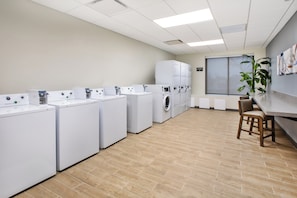 A laundry facility with multiple washing machines and dryers, a wooden floor, and a seating area with a plant. - Candlewood Suites Cincinnati Northeast - Mason (Mason)