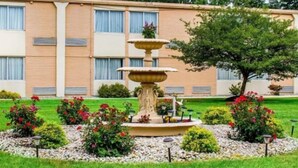 Una fuente de varios niveles en un jardín ajardinado, con un edificio al fondo.
