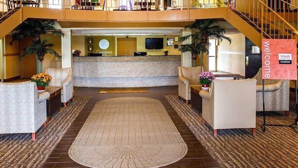 Un vestíbulo de hotel con mostrador de recepción, zona de estar y una escalera que conduce a un nivel superior.