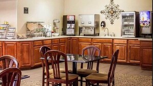 Un comedor con mesa y sillas de madera, cafetera y refrigerador.