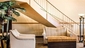 Una sala de estar con sofá, sillón, mesa de centro, escalera y una planta grande.