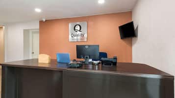 A reception desk with a computer, a flat-screen TV, and a sign that reads 'Quality by Choice Hotels.'