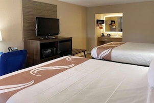 Habitación de hotel con dos camas, televisión, escritorio y espejo.