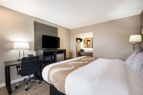 A hotel room with a bed, desk, chair, television, microwave, and a bathroom mirror. - Quality Inn Gastonia East (Gastonia)