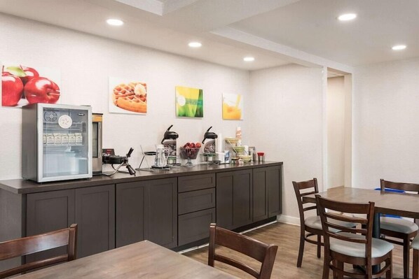 Una cocina moderna con refrigerador empotrado, cafetera y frutero. Hay sillas de madera y una mesa en la zona de comedor.