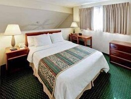 Una habitación de hotel con una cama, dos mesitas de noche, un aparador y una ventana con cortinas.