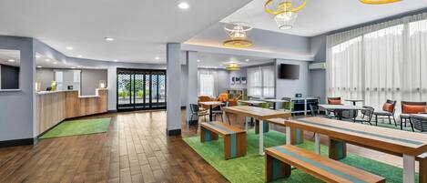 A spacious hotel lobby with wooden flooring, green carpets, and modern furniture.