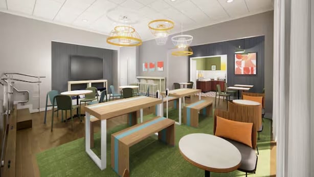 Un espace intérieur moderne doté de plusieurs tables et de bancs, d’une moquette verte et de luminaires au plafond.