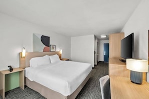 A hotel room with a bed, bedside tables, a TV, and a desk with a lamp. - Spark by Hilton Spring Lake Fayetteville (Spring Lake)