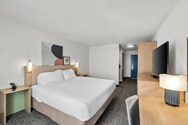 Ein Hotelzimmer mit einem Bett, Nachttischen, einem Fernseher und einem Schreibtisch mit einer Lampe.