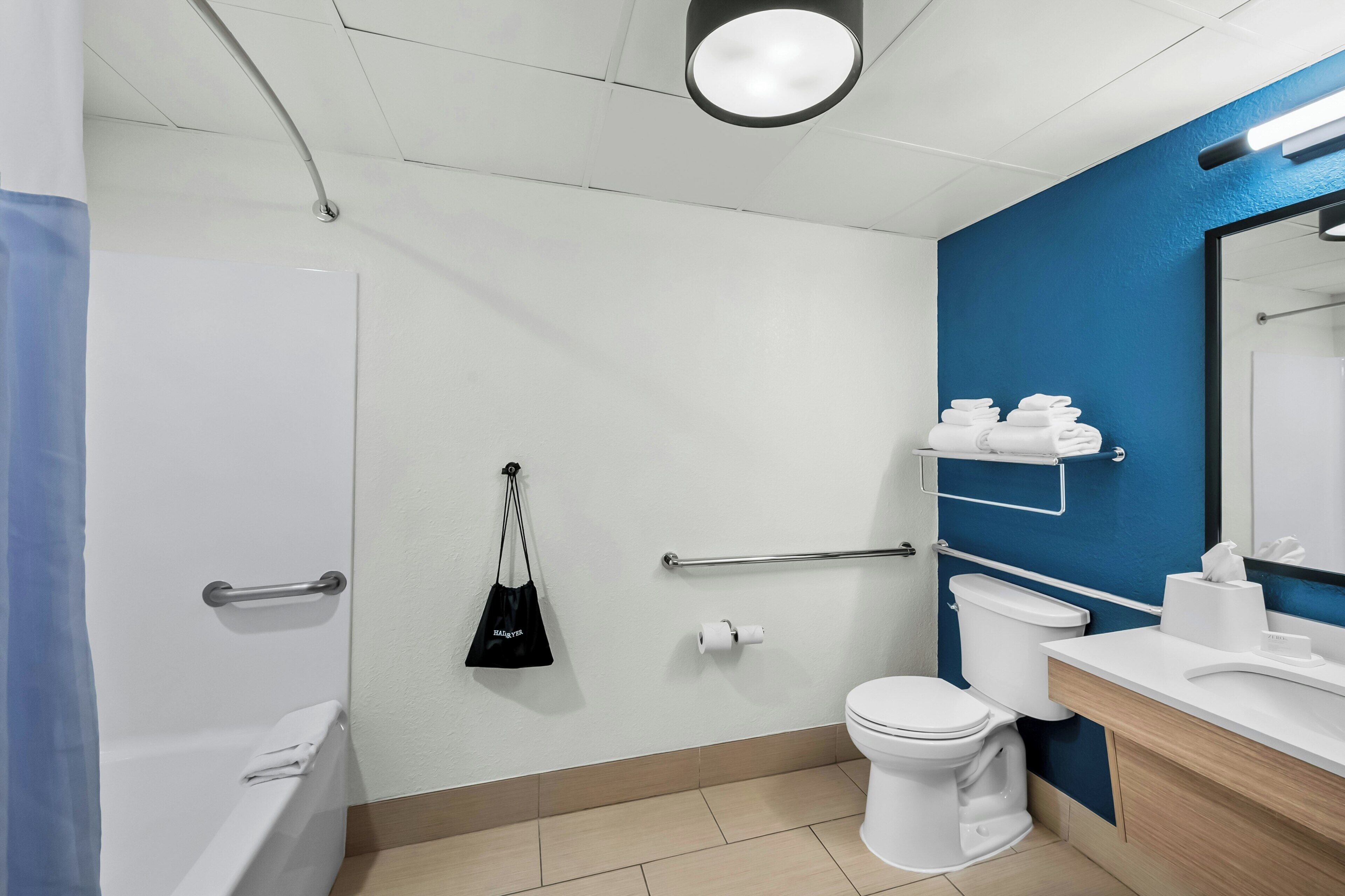 A modern bathroom with a bathtub, toilet, and sink, equipped with handrails and a towel rack.