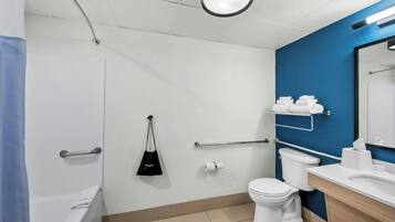 A modern bathroom with a bathtub, toilet, and sink, equipped with handrails and a towel rack.