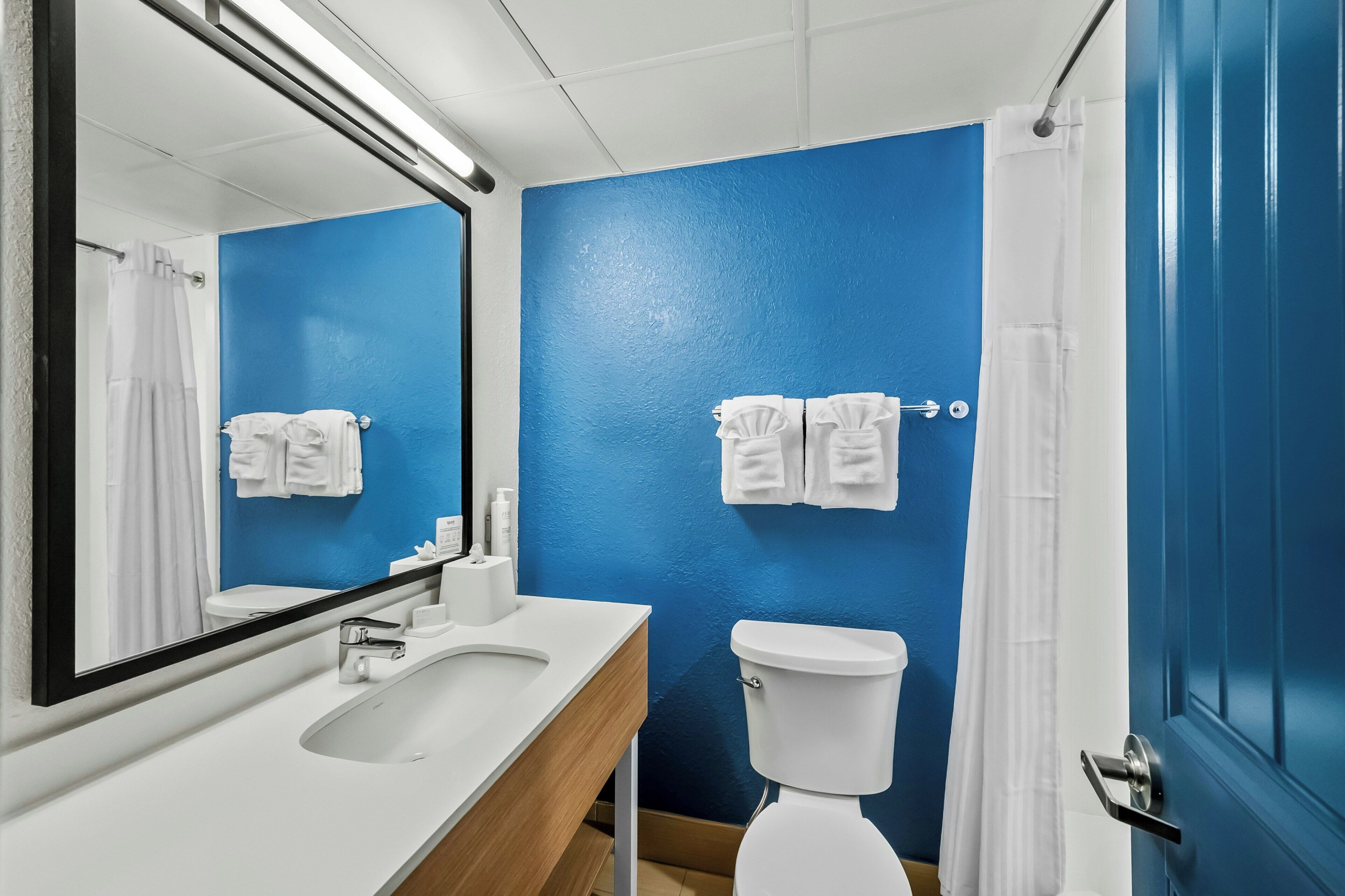 A bathroom with a blue wall, white toilet, and a sink with a mirror.