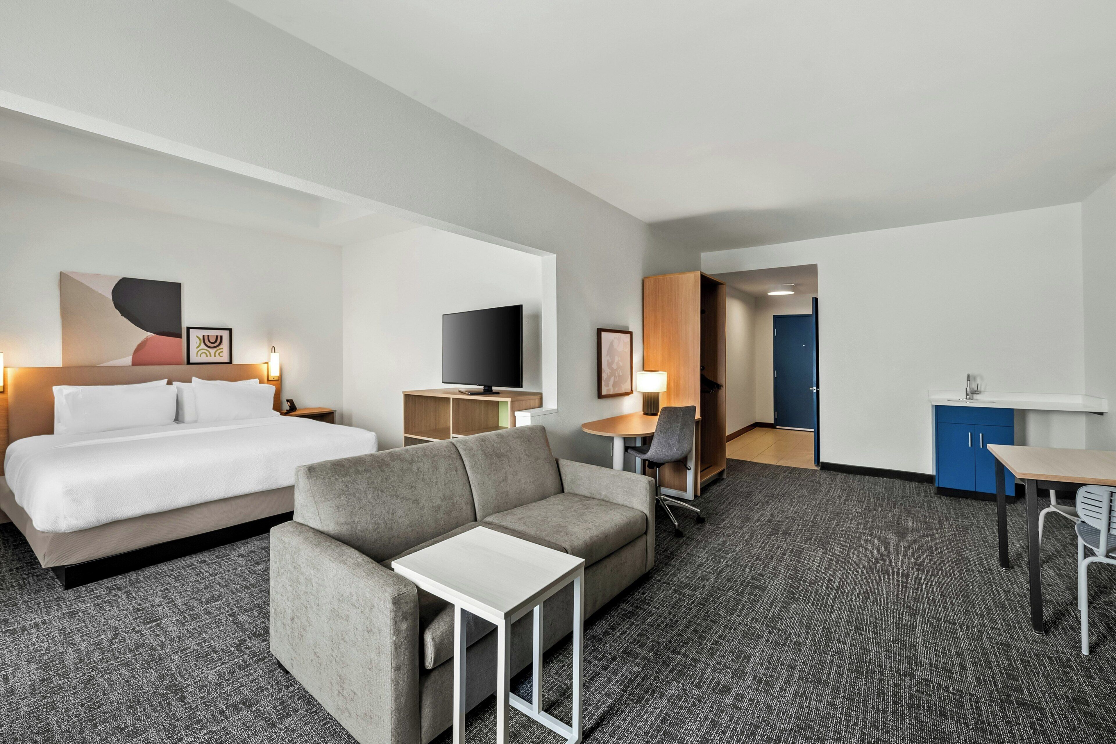 Ett hotellrum med en säng, soffa, TV, skrivbord och ett litet kök.