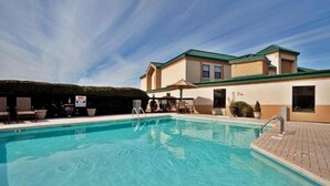 Une piscine avec des chaises longues et des parasols, un bâtiment doté d’un toit végétalisé et un ciel dégagé.