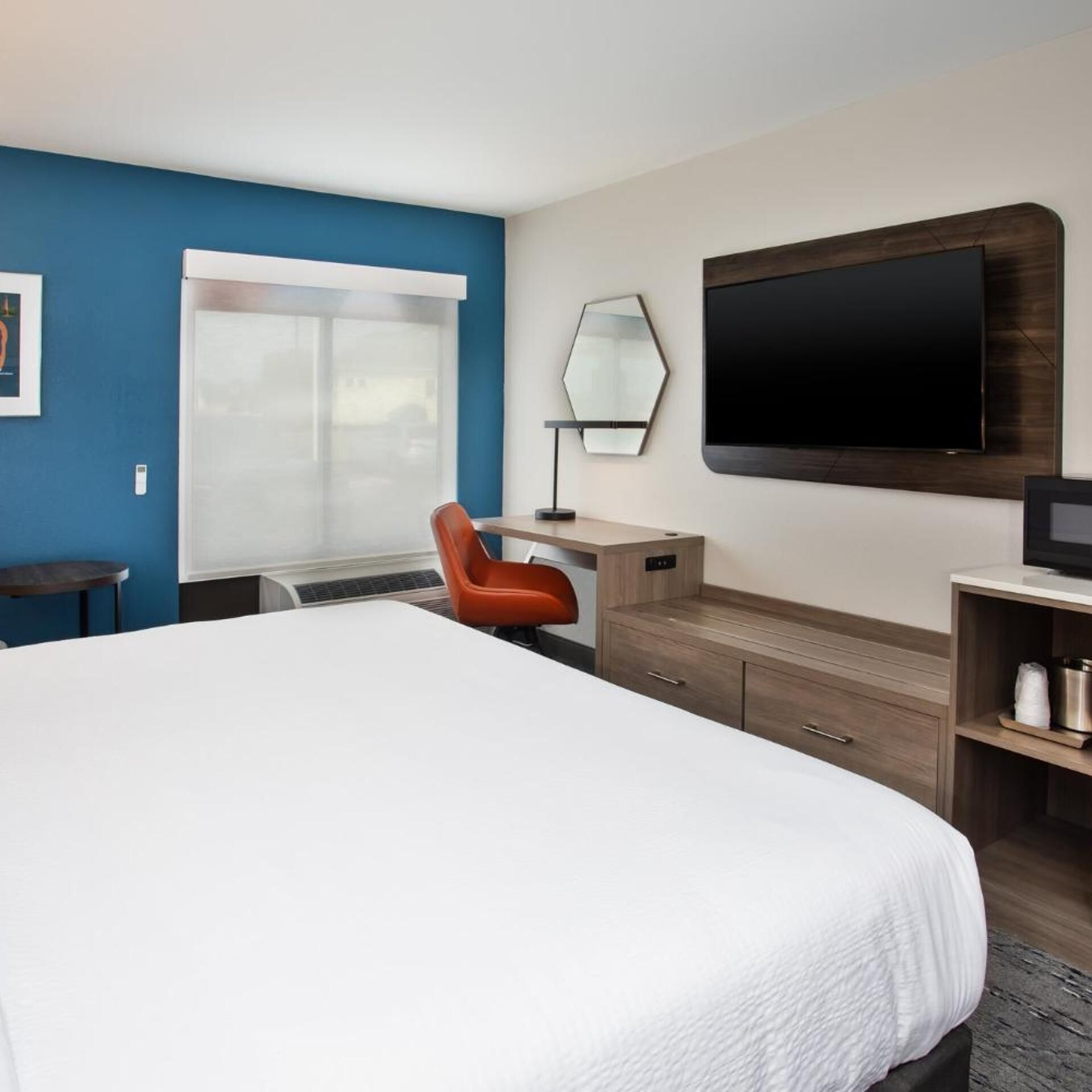 Une chambre d’hôtel avec un grand lit, un bureau avec une chaise, une télévision et une fenêtre avec des stores.
