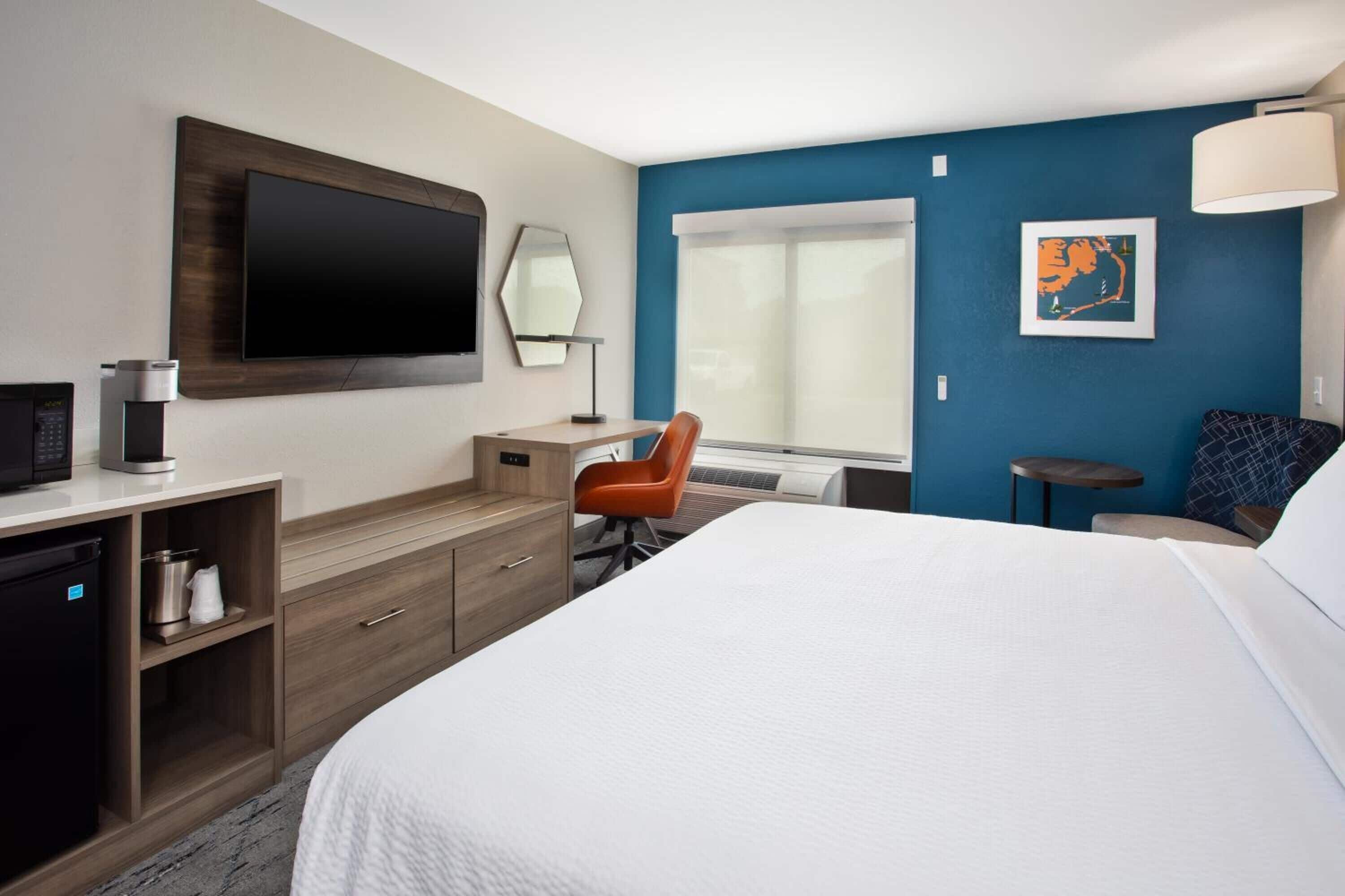 A hotel room with a bed, a desk, a chair, a TV, a coffee machine, and a window.