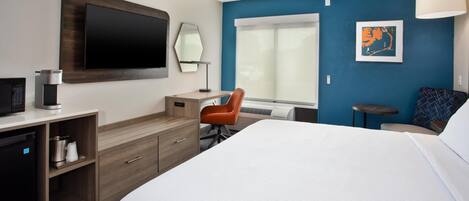 A hotel room with a bed, a desk, a chair, a TV, a coffee machine, and a window.