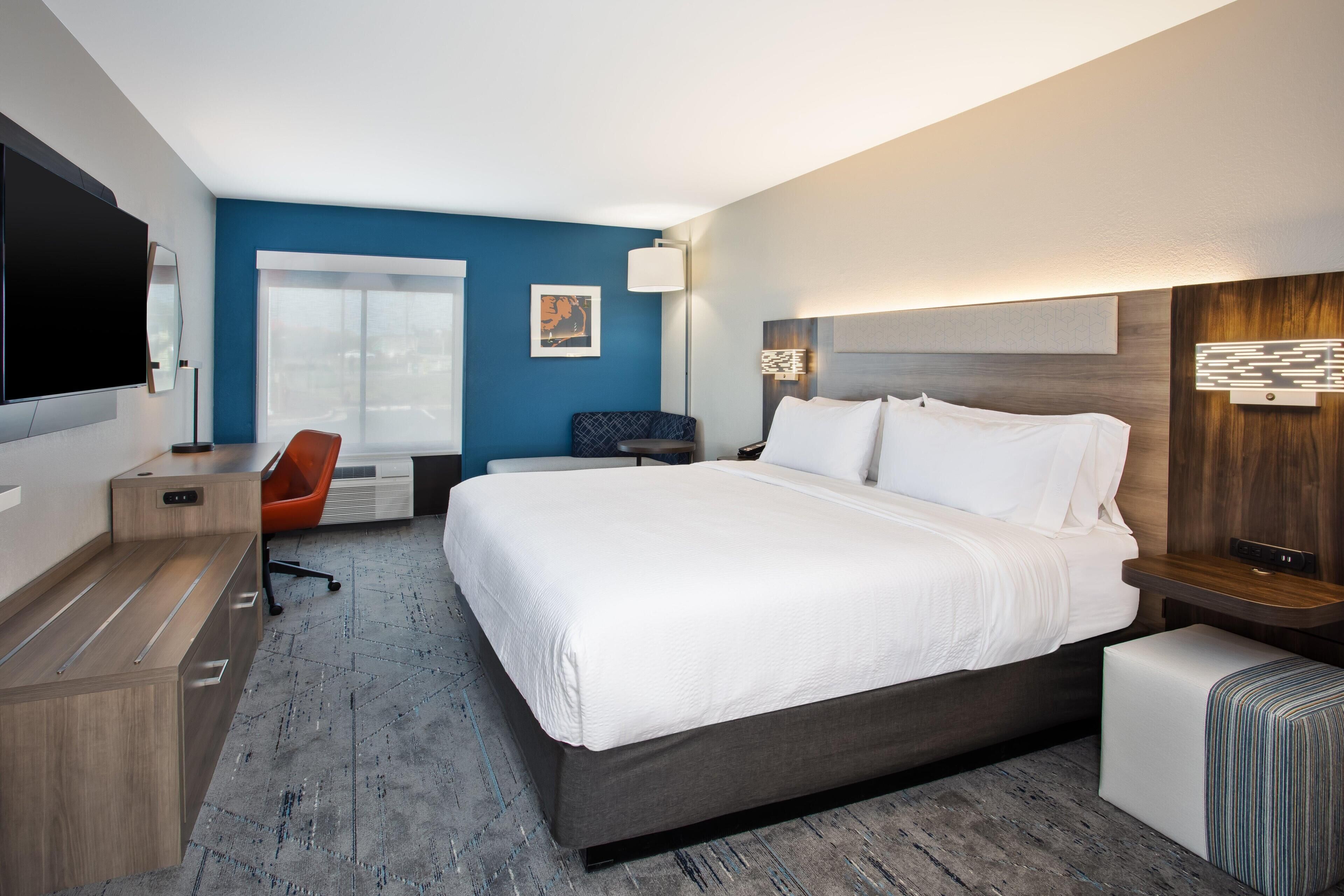 A modern hotel room with a large bed, a desk, a chair, and a flat-screen TV.