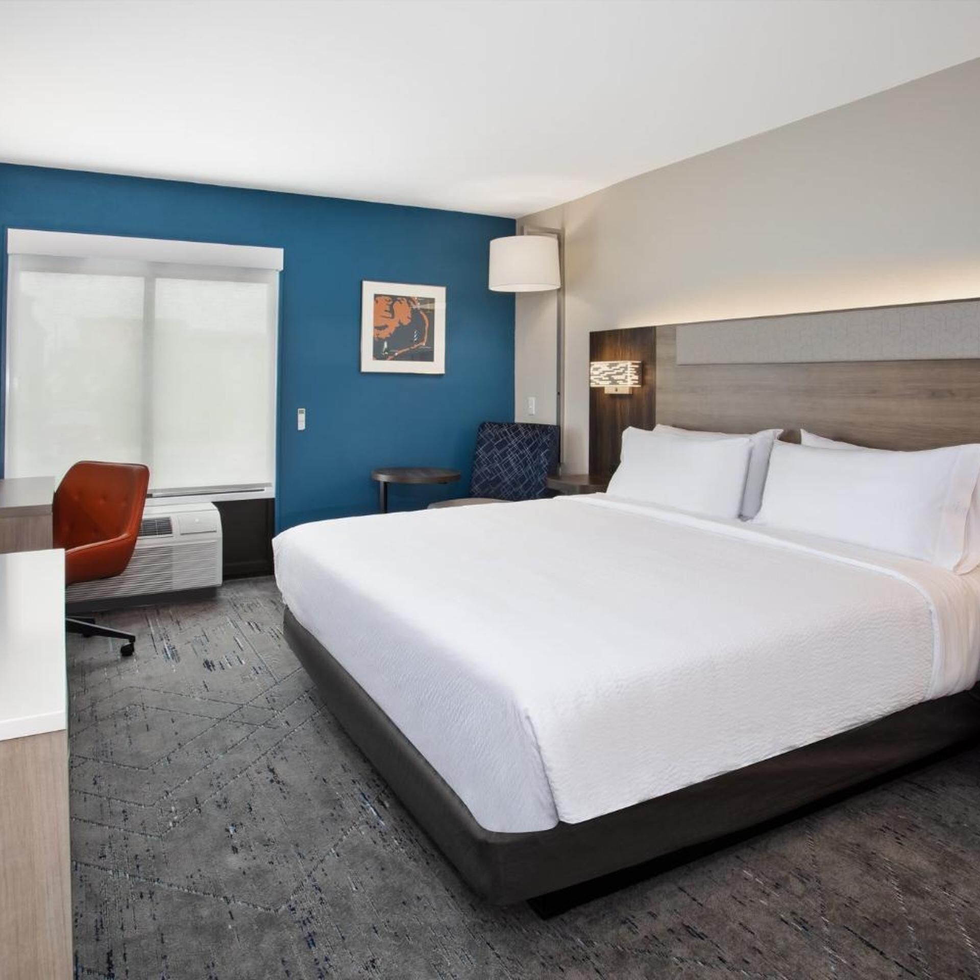 A hotel room with a large bed, a desk, a chair, a window, and a wall-mounted artwork.