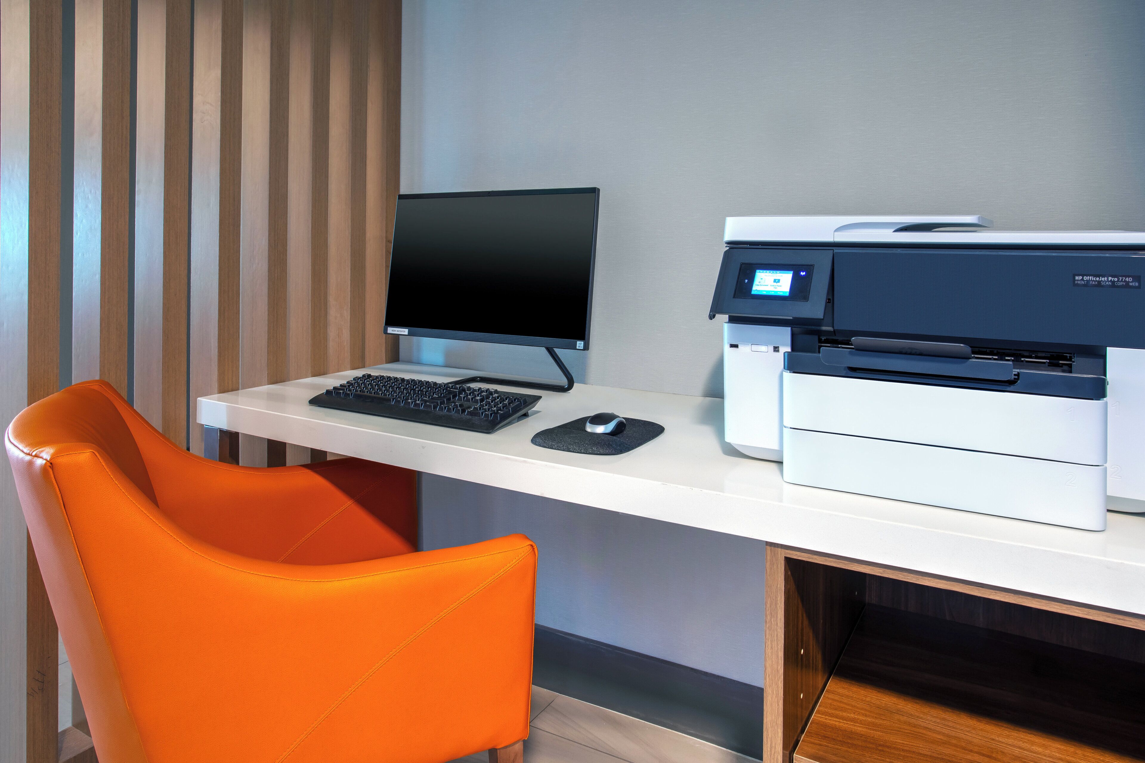 A modern office desk with a computer, printer, and orange chair.