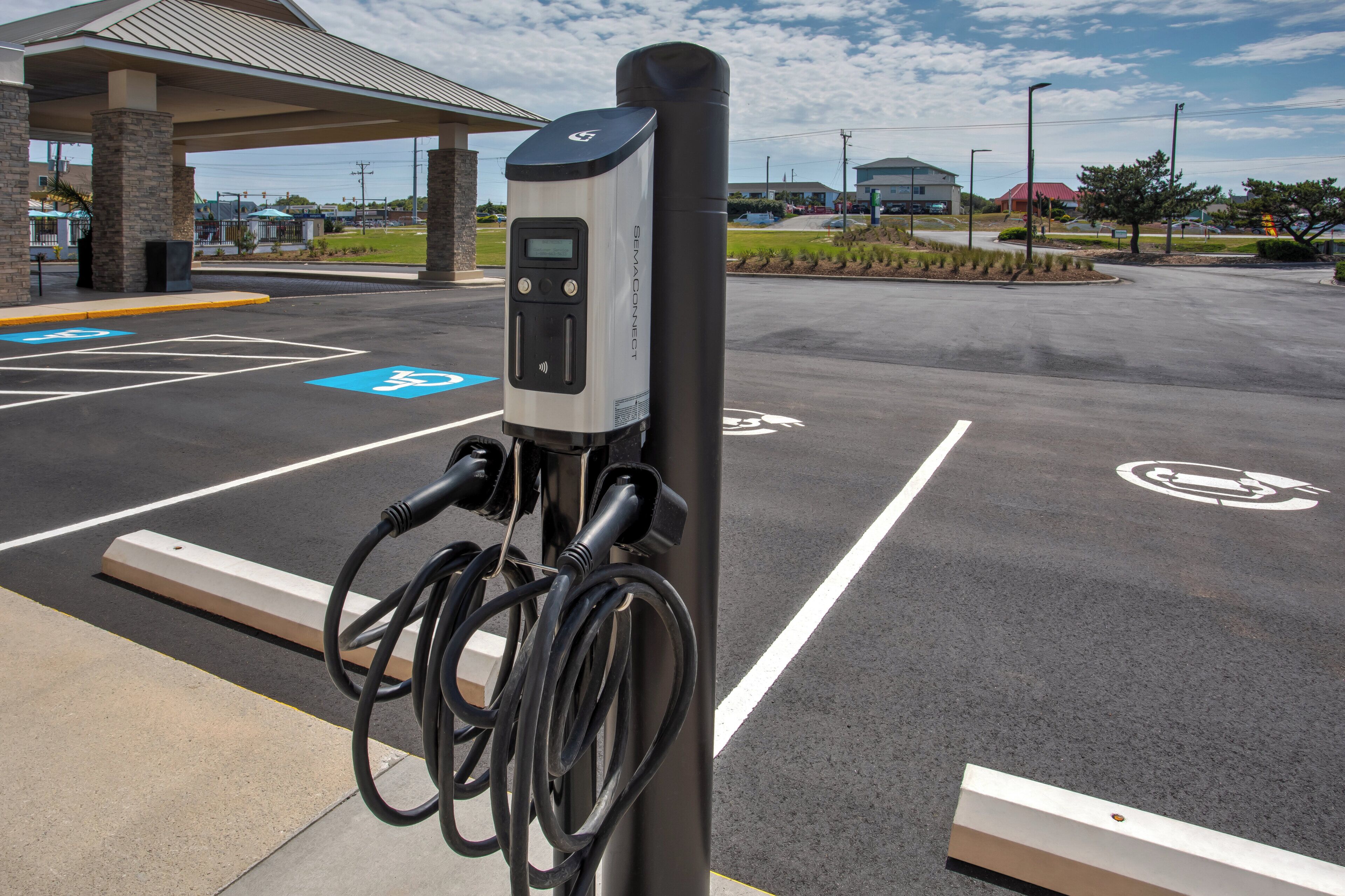 Eine Ladestation mit digitalem Display, verbunden durch Kabel, in einem Parkplatz mit gekennzeichneten Stellplätzen.
