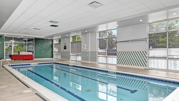 Una piscina interior con agua cristalina, paredes de azulejos y una mesa roja.