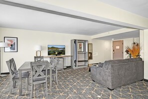 A hotel room with a dining area, a gray sofa, a flat-screen TV, and a patterned carpet. - Holiday Inn Piscataway - Somerset (Piscataway)