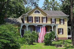 A yellow colonial-style house with a porch, a large American flag, and a tree in the foreground. - Holiday Inn Piscataway - Somerset (Piscataway)