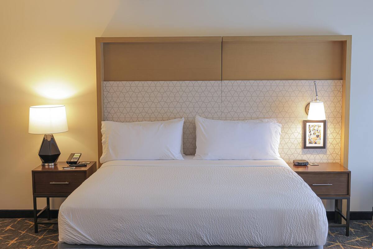 Quarto de hotel com uma cama grande, duas mesas de cabeceira, cabeceira com padrão geométrico e duas luminárias fixadas na parede.