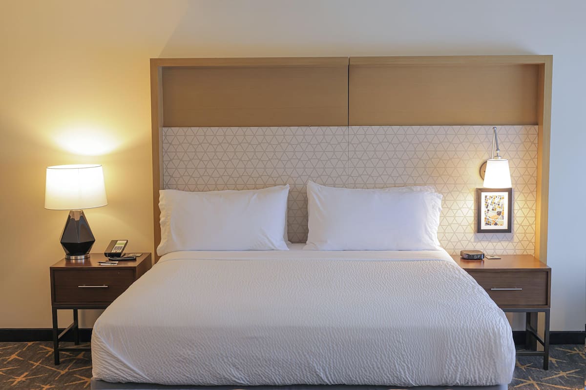 A hotel room with a large bed, two bedside tables, a headboard with a geometric pattern, and two wall-mounted lamps.