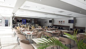 A modern dining area with tables and chairs, a kitchen in the background, and a large plant in the foreground. - Holiday Inn Piscataway - Somerset (Piscataway)