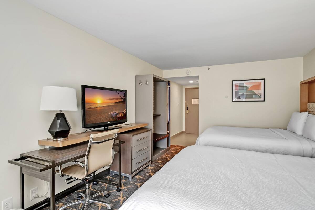 Quarto de hotel com cama, escrivaninha, cadeira, televisão e obras de arte.