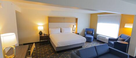 A hotel room with a bed, a desk with a lamp, a sofa, and a chair.