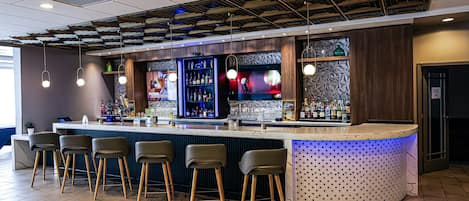 A bar area with a counter, stools, and shelves of bottles.