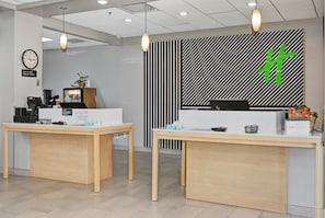 Una reception con una scrivania, un orologio, una pianta e una parete decorata con un simbolo verde.