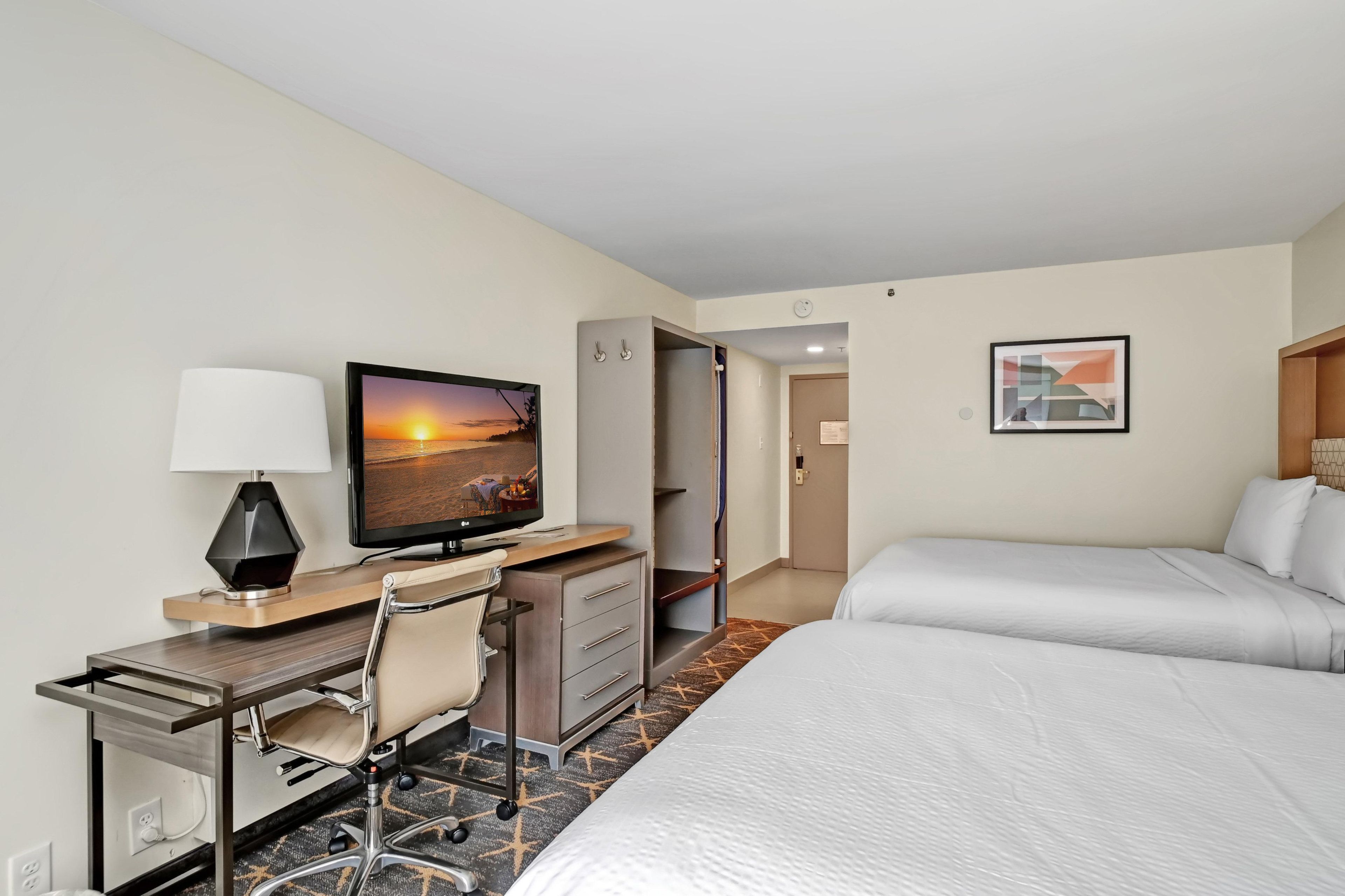 A hotel room with a bed, desk, chair, television, and artwork.