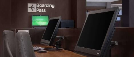 A check-in counter with two computer stations, a keyboard, a mouse, and a monitor displaying a boarding pass.