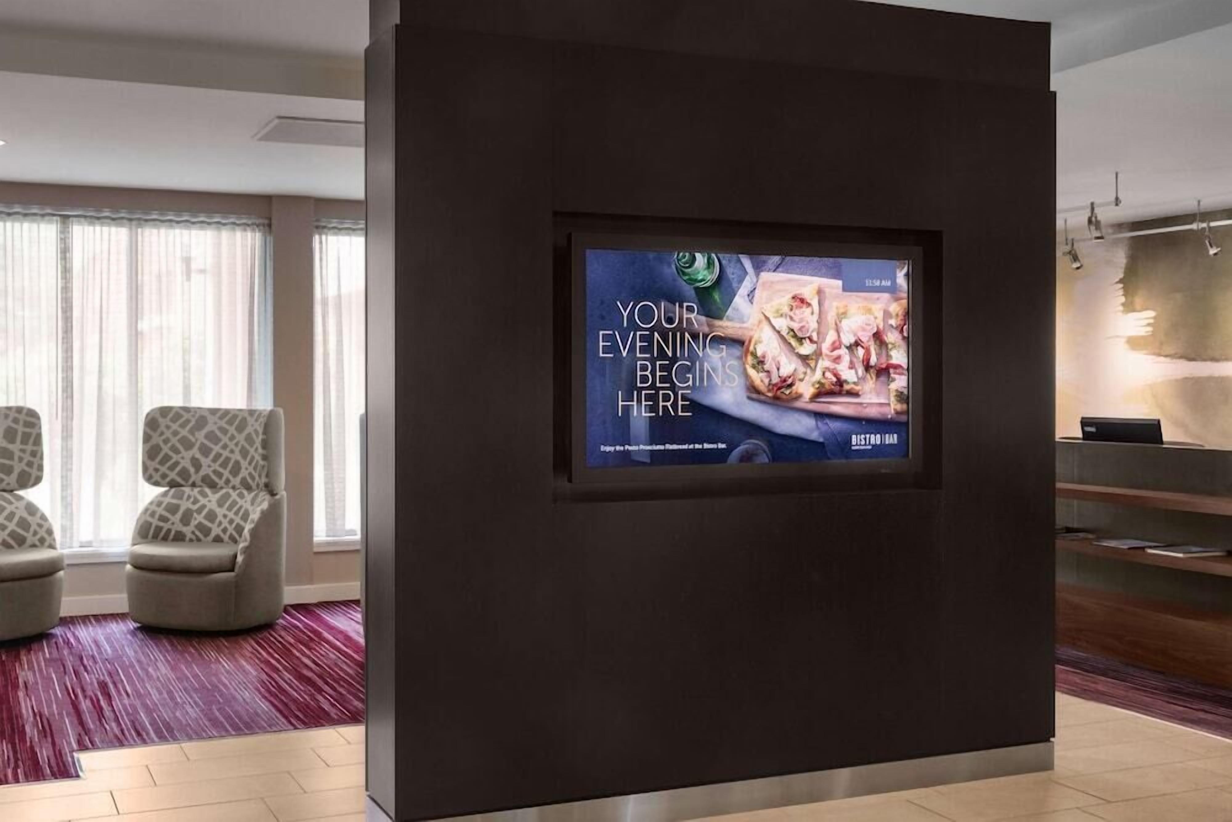 A modern hotel lobby with a large screen displaying a restaurant advertisement.