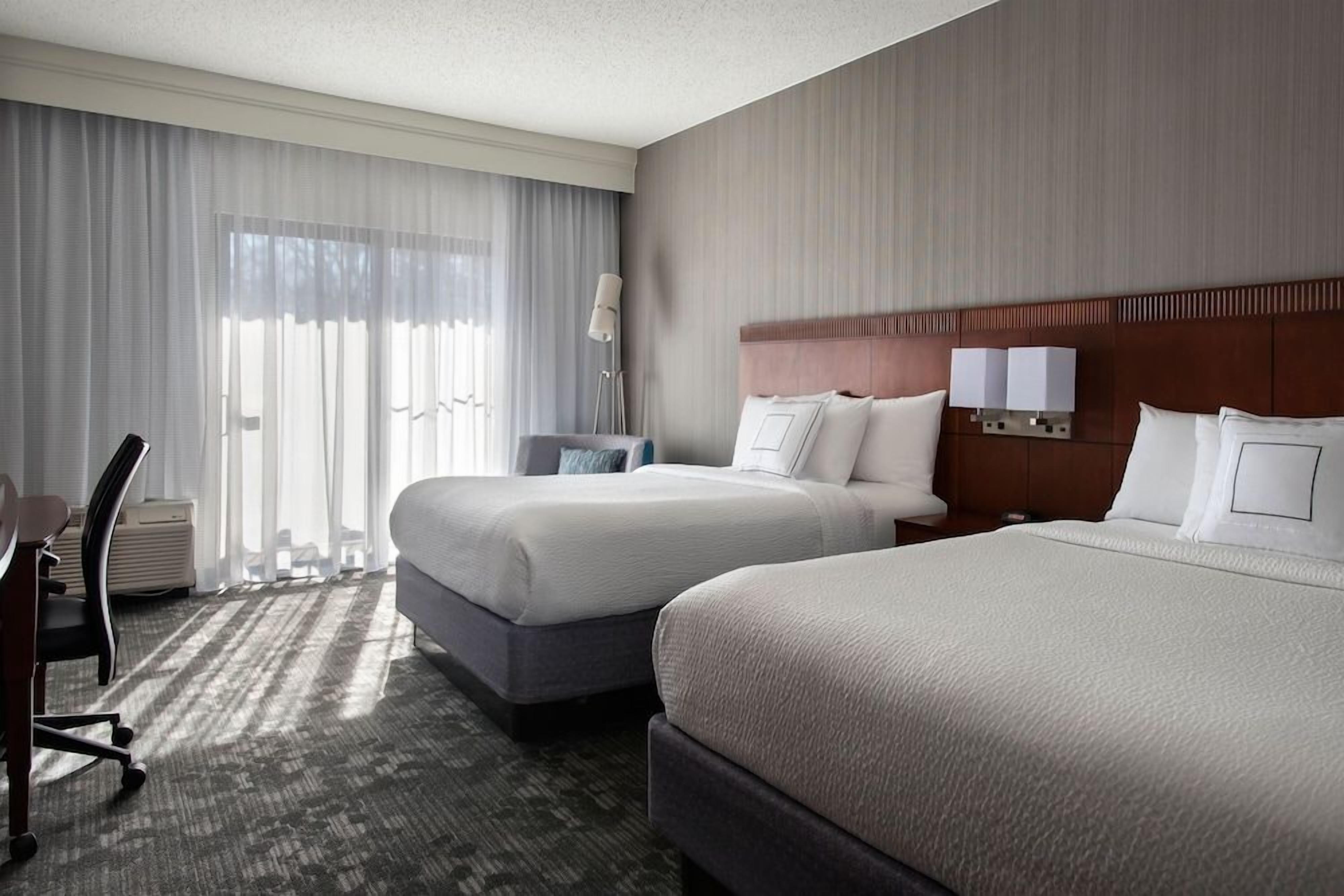 A hotel room with two beds, a desk, and a chair.