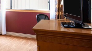A hotel room with a wooden desk, a television, a chair, a window with curtains, and a red wall. - Toms River (Toms River)