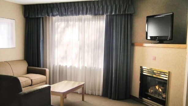 A hotel room with a sofa, a small table, a fireplace, and a TV mounted on the wall. - Toms River (Toms River)