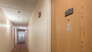 Un couloir d’hôtel avec un tapis à motifs, une porte en bois portant le numéro de la chambre, et un panneau indiquant que l’établissement est non-fumeur et accepte les animaux de compagnie.