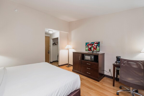 Une chambre d’hôtel équipée d’un lit, d’un bureau avec un ordinateur, d’une télévision, d’un four à micro-ondes et d’une machine à café.