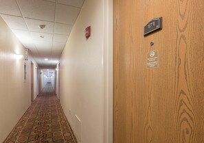Un couloir d’hôtel avec un tapis à motifs, une porte en bois portant le numéro de la chambre, et un panneau indiquant que l’établissement est non-fumeur et accepte les animaux de compagnie.