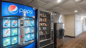 Un distributeur automatique aux couleurs de Pepsi, proposant une sélection de boissons, situé à côté d’un réfrigérateur rempli d’en-cas.